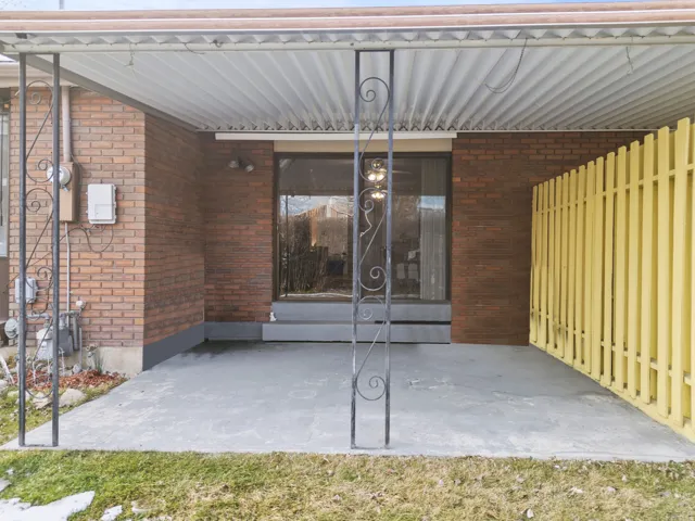 Covered patio space featuring a concrete slab, brick exterior, metal roof, and decorative ironwork columns