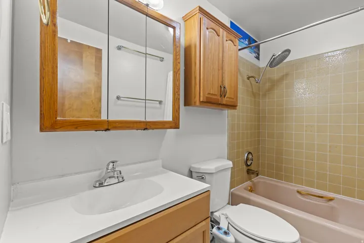 Bathroom with a single vanity, wood-finish medicine cabinet, overhead lighting, and a shower/tub combination with beige tiled walls