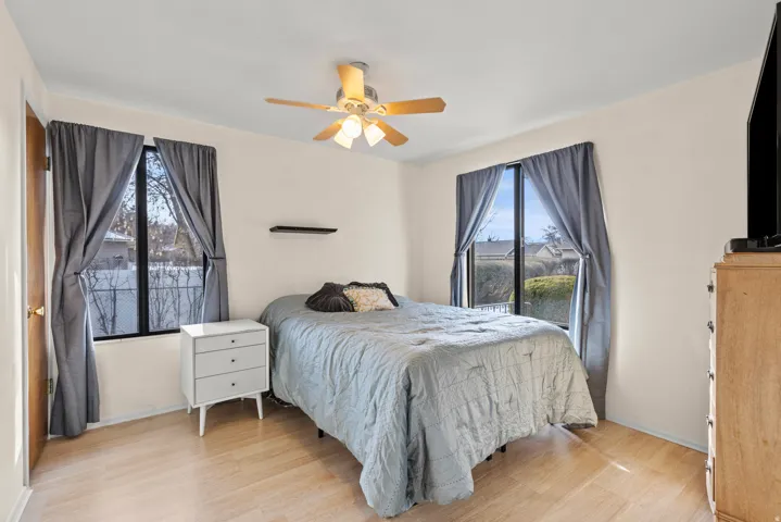 Wood-finish flooring, two large windows, ceiling fan with integrated lighting, and a wall-mounted shelf
