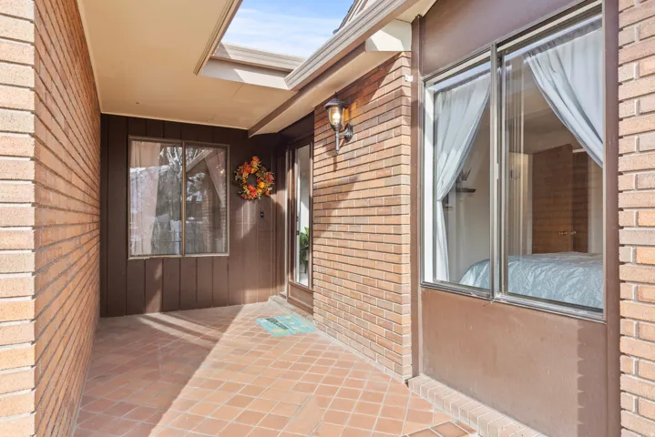 Brick exterior with a covered entry, terracotta tile flooring, and exterior wall sconce