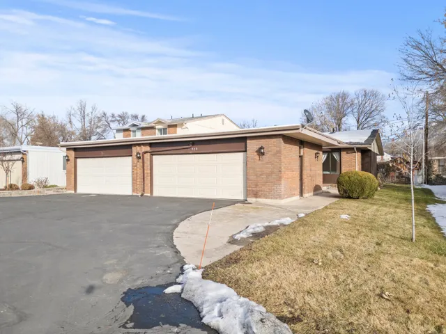 Brick exterior with two attached garages, paved driveway, and established landscaping
