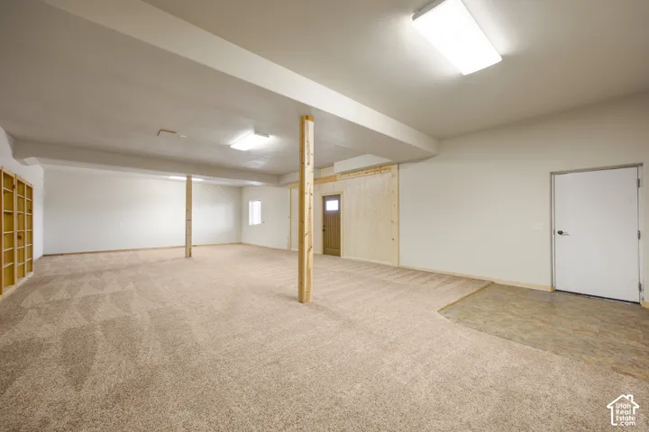 Expansive carpeted area with exposed support beams, recessed lighting, and a window