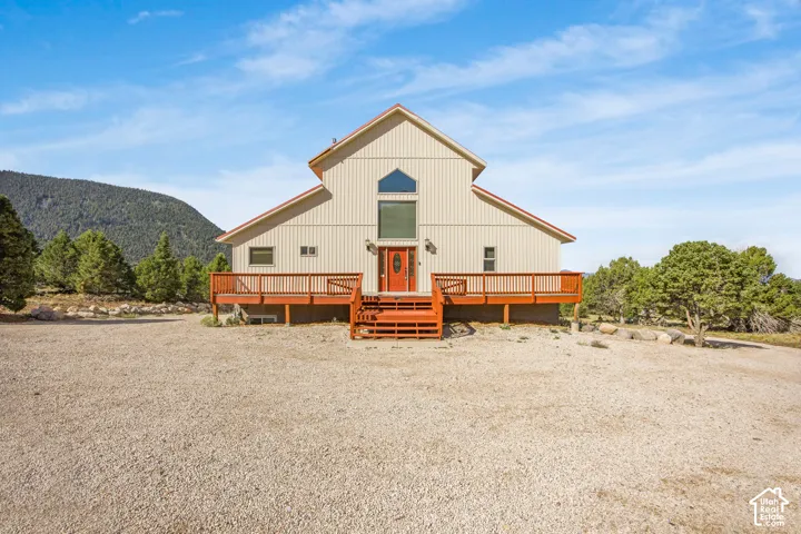 Gable roofline, beige siding, red entry door, expansive wooden deck with railings, natural mountain backdrop
