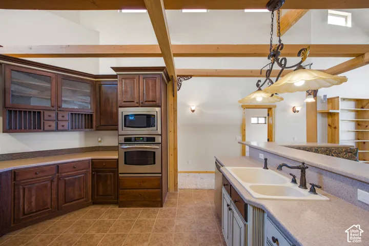 Kitchen featuring rich wood cabinetry, stainless steel built-in appliances, a double basin sink, and exposed wood beams