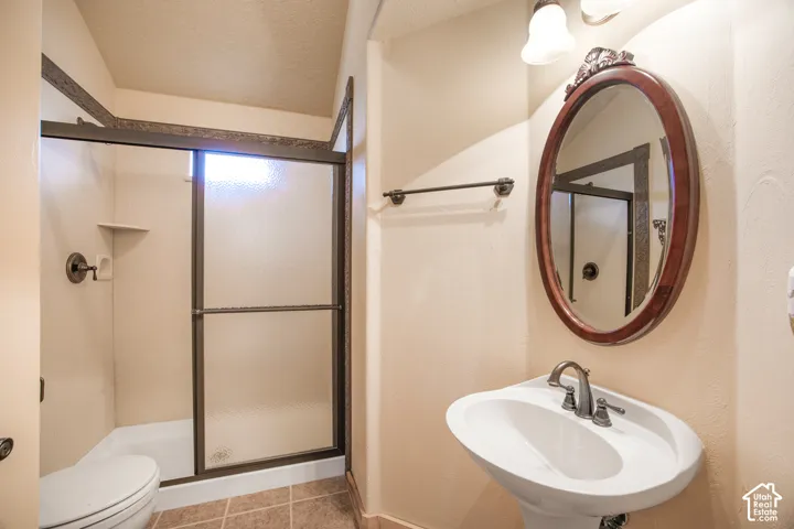 Pedestal sink with a two-handle faucet, oval mirror with a decorative frame, and a shower with sliding opaque glass doors