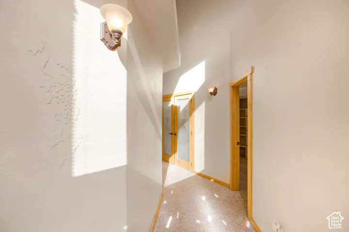 Hallway featuring textured walls, a decorative wall sconce, natural wood door frames, and a built-in shelving unit