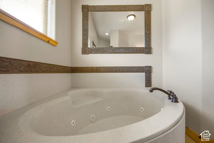 Corner jetted tub with integrated steps, bronze-finish faucet, and coordinating wall trim