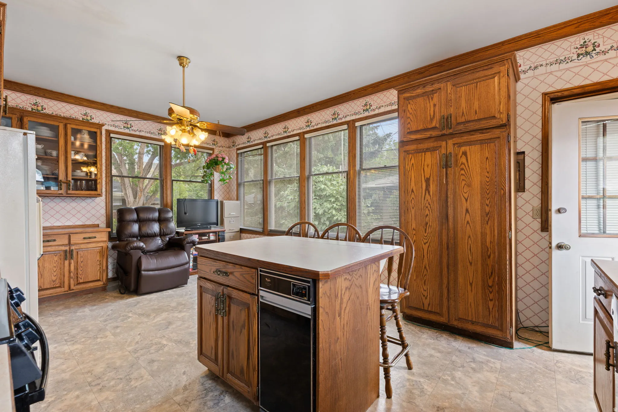 Wood-finish cabinetry, tile backsplash, white countertops, built-in island with integrated appliance, and vinyl flooring