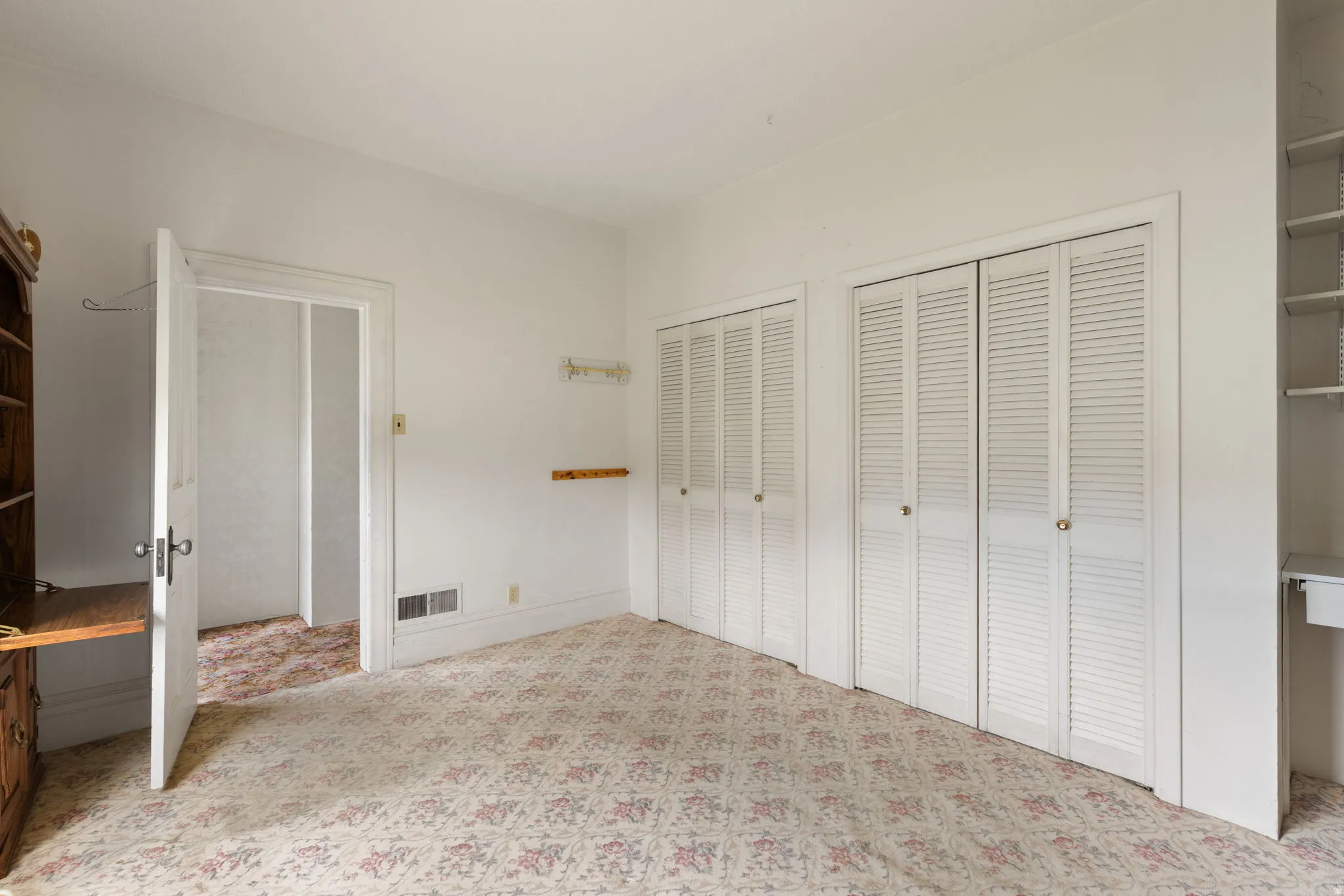 White louvered bi-fold doors, built-in shelving, wood-finish built-in desk, and a painted paneled door