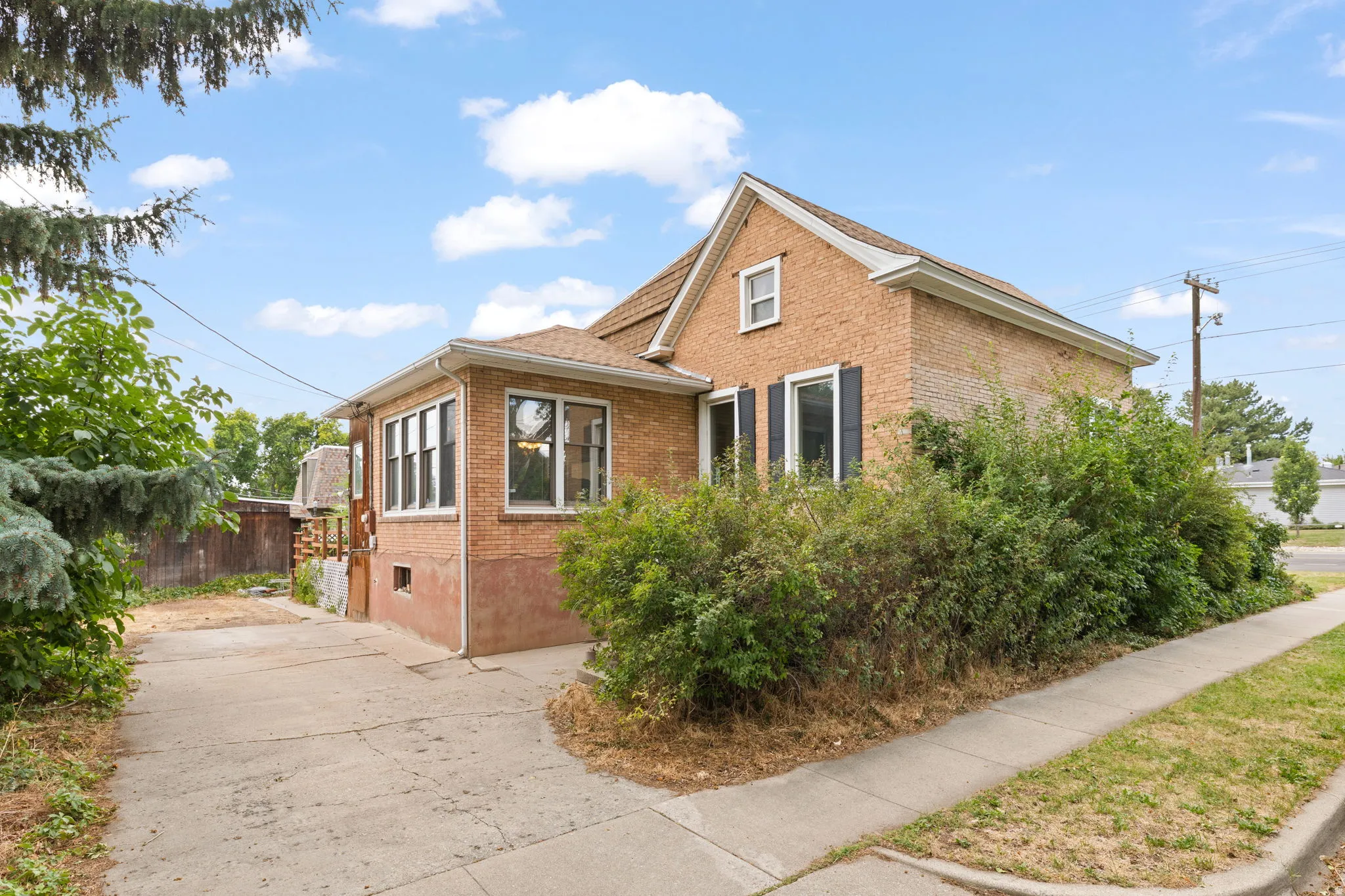 Brick exterior construction, multiple windows, gabled roofline, concrete driveway, and established perimeter landscaping