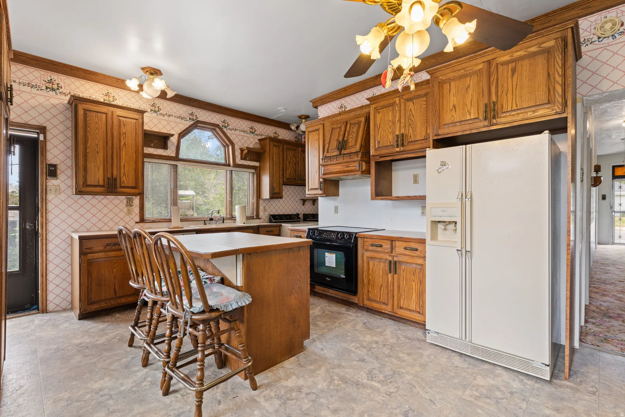 Kitchen featuring wood cabinetry, an integrated island, white countertops, a black range, and a white side-by-side refrigerator