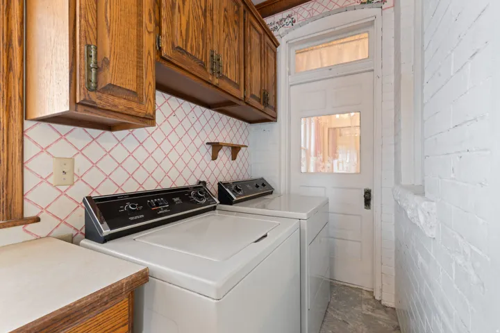 Wood cabinetry, laminate countertop, patterned tile backsplash, painted brick wall, and a white paneled door with transom window