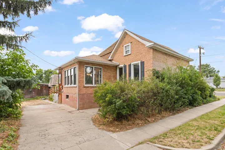 Brick exterior construction, multiple windows, gabled roofline, concrete driveway, and established perimeter landscaping
