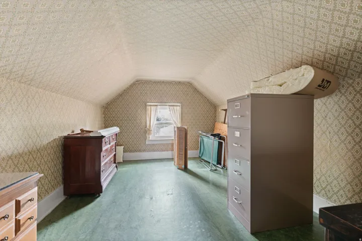 Room featuring sloped ceilings, patterned wallpaper, a window with curtains, and green-painted flooring
