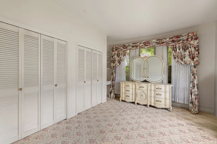 Dual louvered closet doors, wall-to-wall carpeting, and multiple windows with vertical blinds