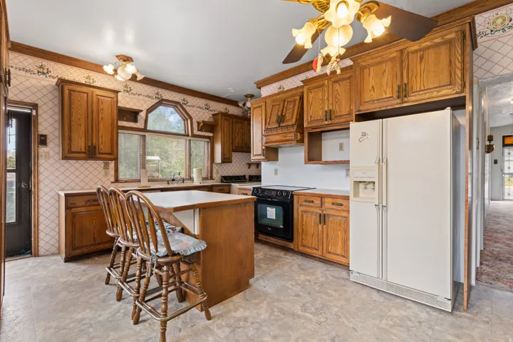 Kitchen featuring wood cabinetry, an integrated island, white countertops, a black range, and a white side-by-side refrigerator