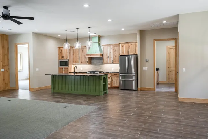 Kitchen featuring wood-finish cabinetry, a green island with a dark countertop, stainless steel appliances, and pendant lighting