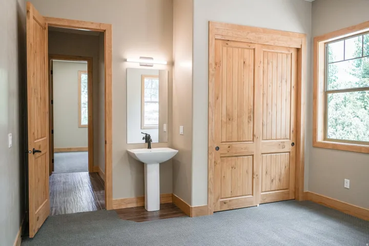 Pedestal sink with wall-mounted mirror, wood-paneled sliding doors, natural wood trim, and a large window