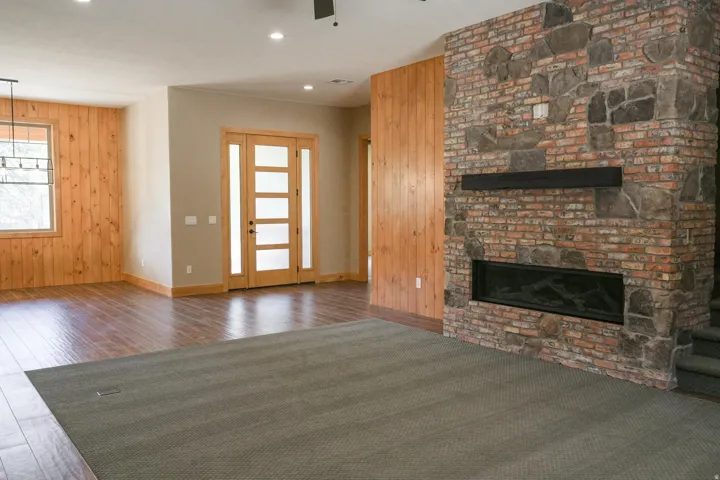 Stone and brick fireplace with a linear insert, wood-finish flooring, wood paneling, and an entry door with frosted glass panels