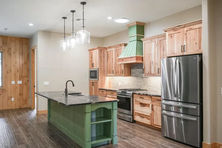 Gourmet kitchen featuring a green island with dark countertop, stainless steel appliances, wood cabinetry, stone backsplash, and wood-finish flooring