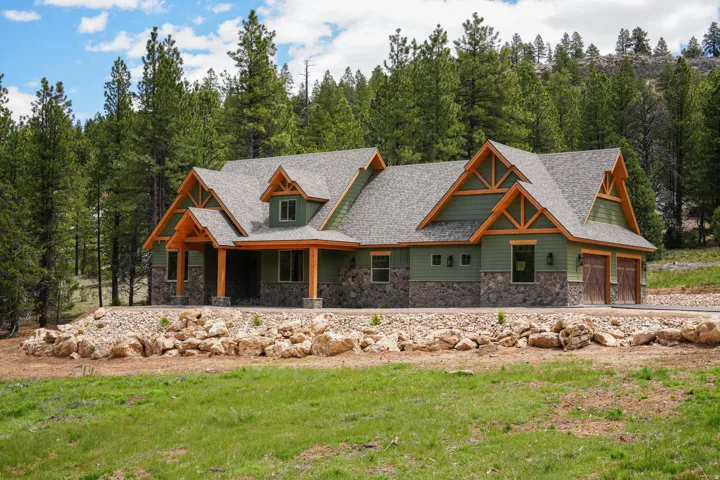Craftsman-style home featuring a green siding exterior, stone accents, natural wood trim, and a multi-gabled roofline