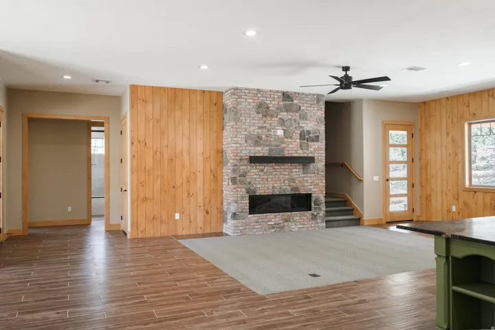 Stone and brick fireplace with an integrated modern firebox, wood-finish flooring, wood panel accent wall, recessed lighting, and a ceiling fan