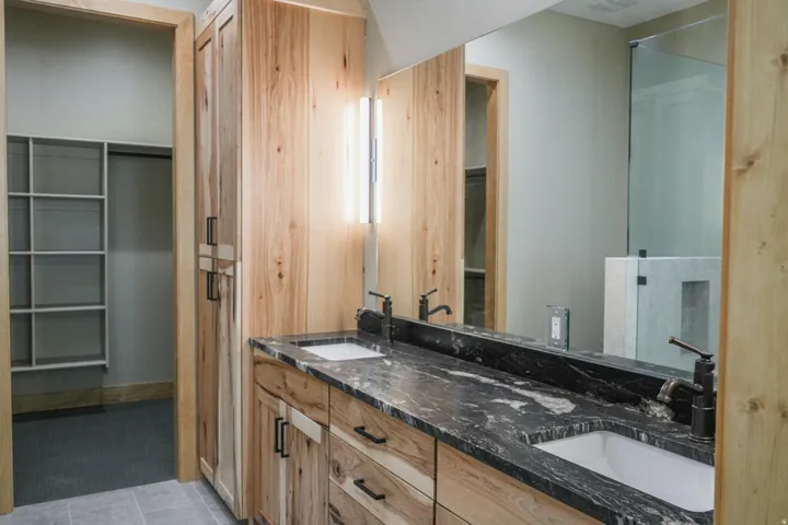 Dual vanity with dark stone countertop, undermount sinks, and wood-finish cabinetry