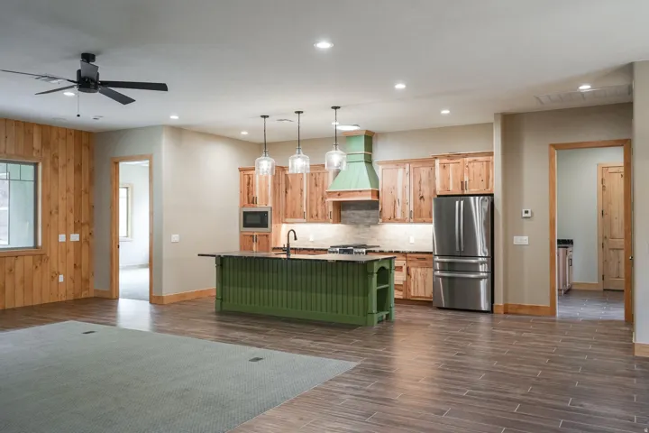 Open-concept kitchen with wood-finish flooring, a central island featuring a sink and cooktop, and stainless steel appliances