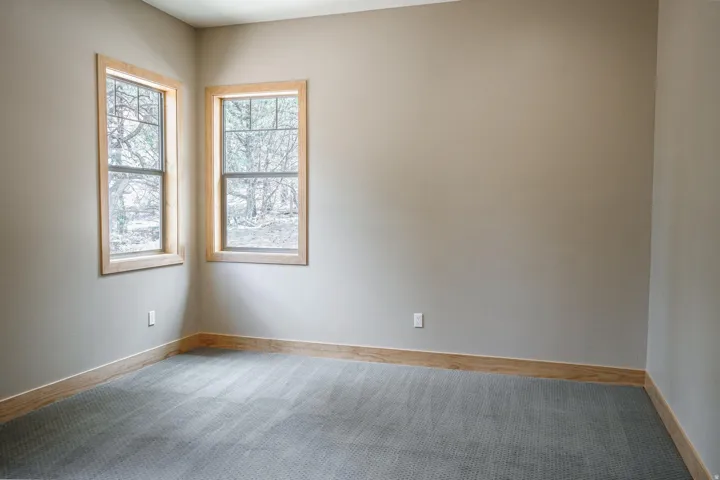 Corner windows with natural wood trim, plush carpet flooring, and neutral wall tones
