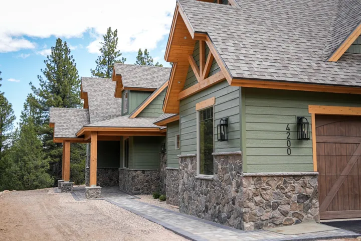 Craftsman-style home featuring a green siding exterior with stone accents, exposed wood beams, a covered entryway, and an asphalt shingle roof