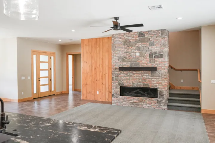 Stone and brick fireplace with an electric insert, wood-finish flooring, and a ceiling fan