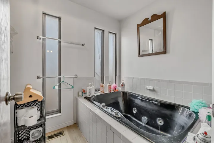 Built-in soaking tub with white tile surround, accompanied by vertical frosted windows and chrome towel bars