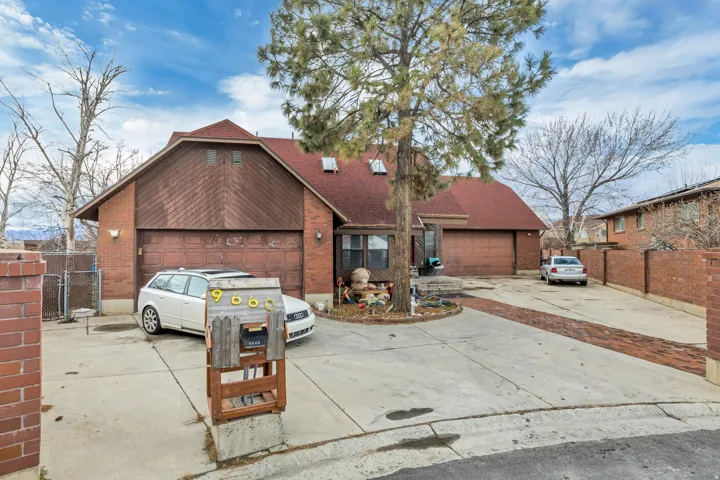 Brick and wood-sided exterior featuring multiple garage doors, a red-toned shingle roof, and a mature tree in the front yard