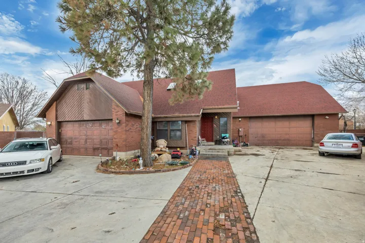 Brick exterior with a reddish-brown shingle roof, featuring two garage doors and a paved driveway with a brick-laid pathway
