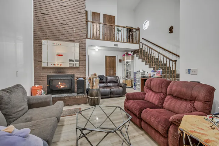 Two-story living area featuring a brick fireplace, wood-finish flooring, a wood-railed staircase, and a second-story balcony with wood railings