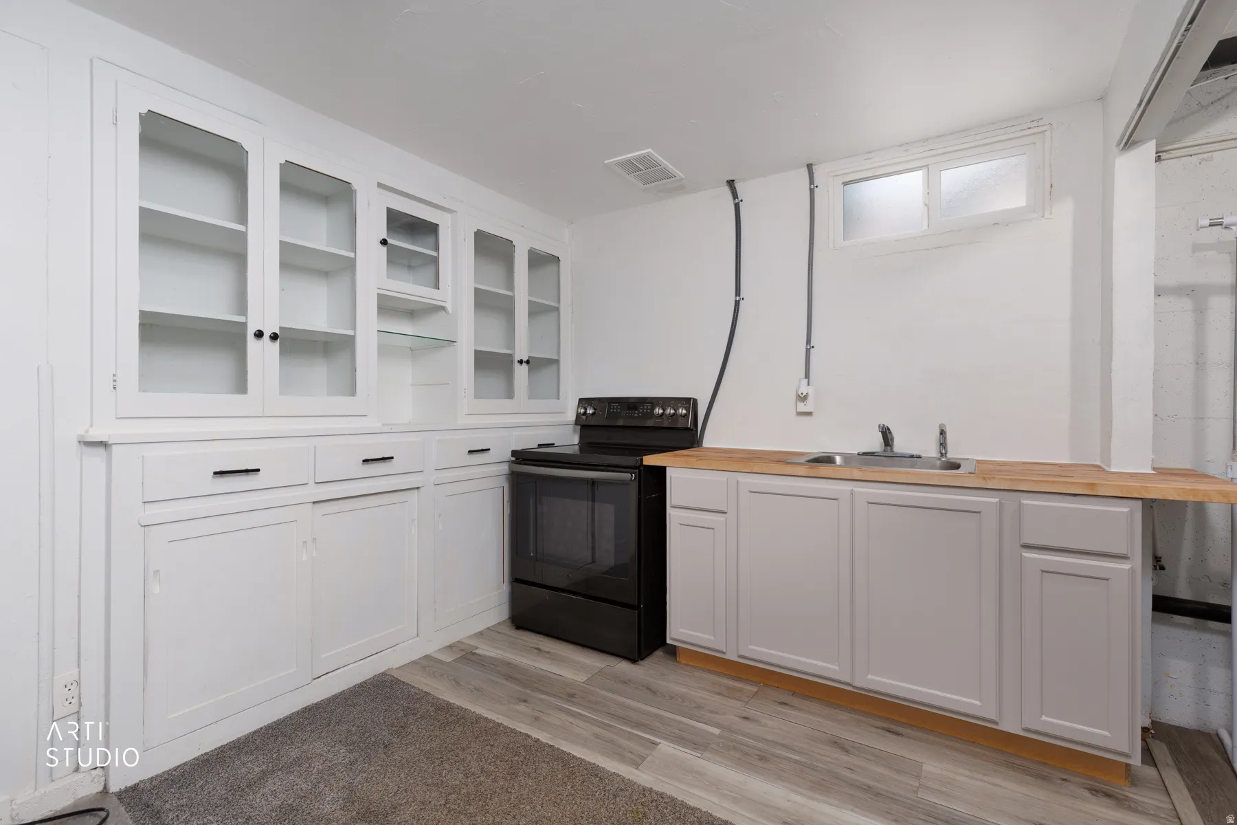 Built-in white cabinetry with glass display doors, matte black range, stainless steel sink, wood-finish countertop, and wood-finish flooring