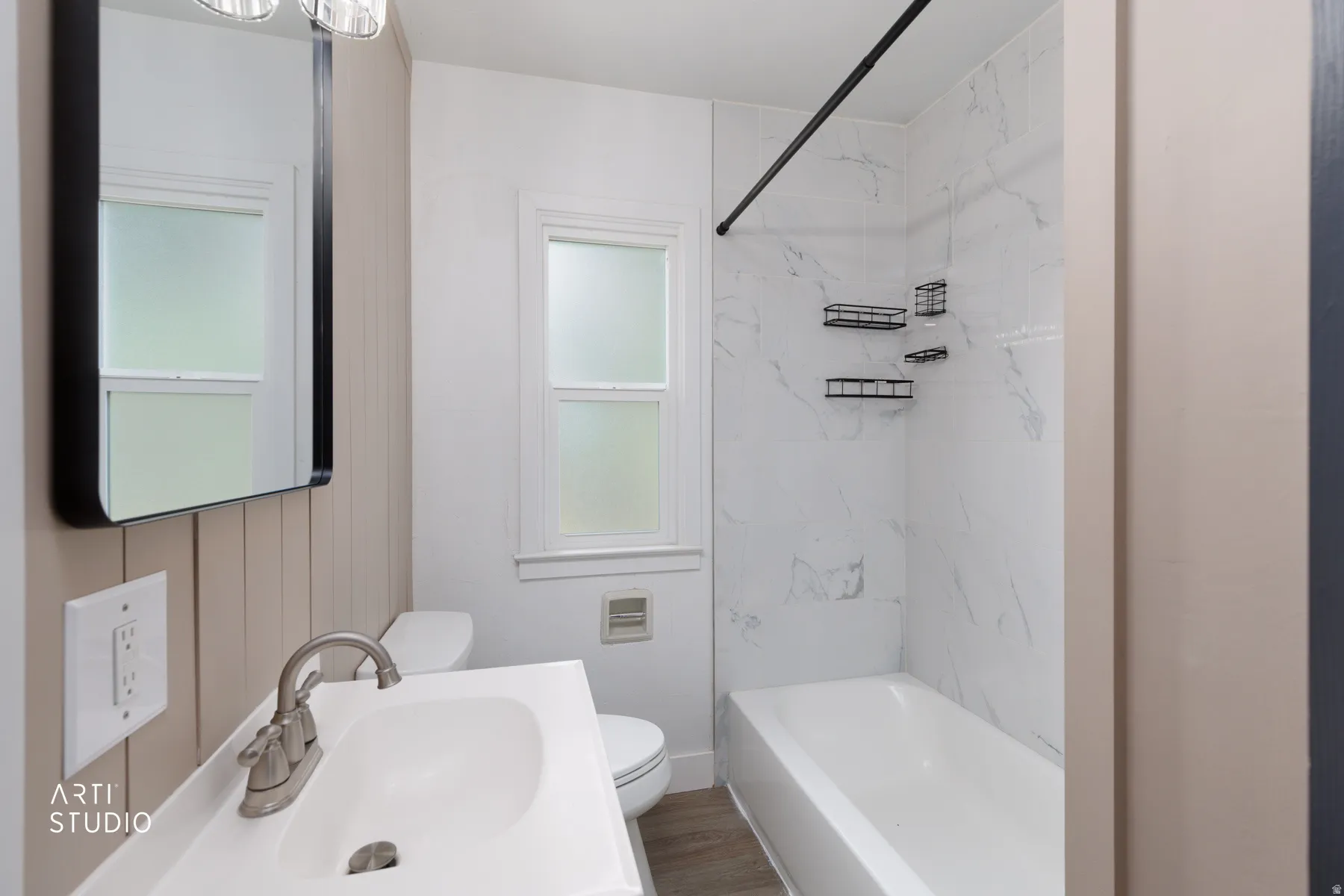 Bathroom featuring a shower-tub combination with white marble-look paneling, a wall-mounted shower rod, a vanity with an integrated sink, and an unframed mirror