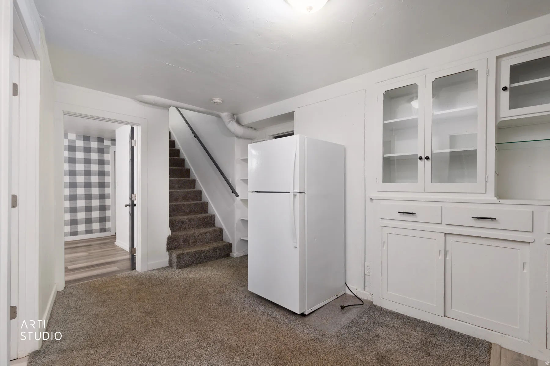 Built-in cabinetry with glass-front doors, neutral carpeting, and a stairway with a dark handrail