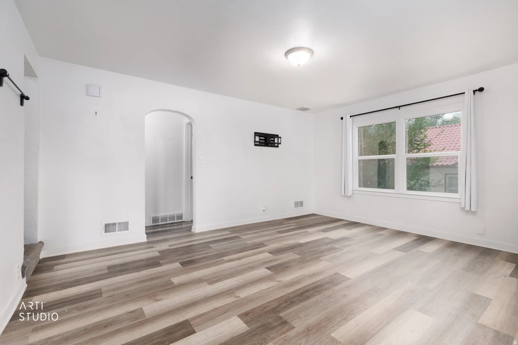 Wood-finish flooring throughout, white painted walls, window with black curtain rod, recessed lighting, and an arched doorway