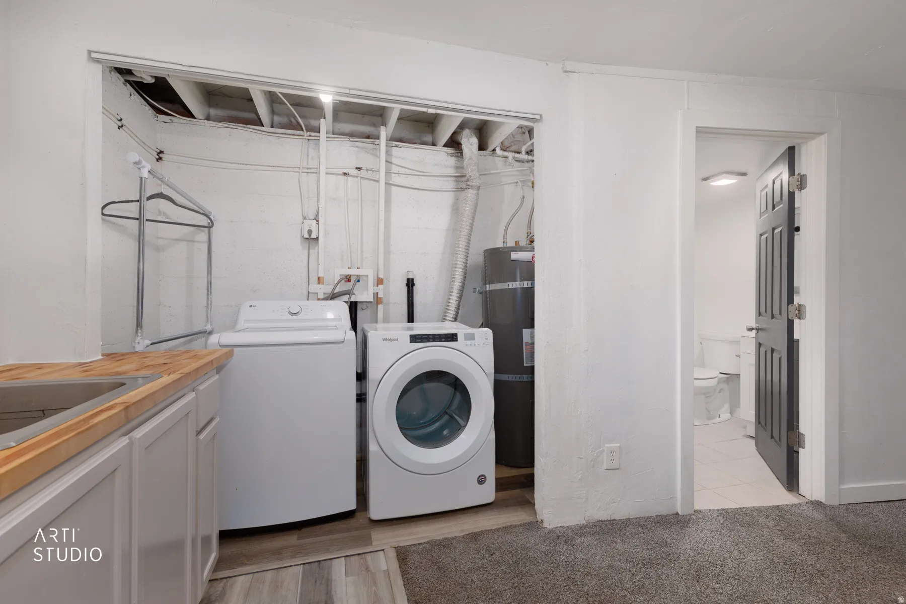 Integrated laundry area featuring wood-finish countertop, utility sink, and built-in cabinetry