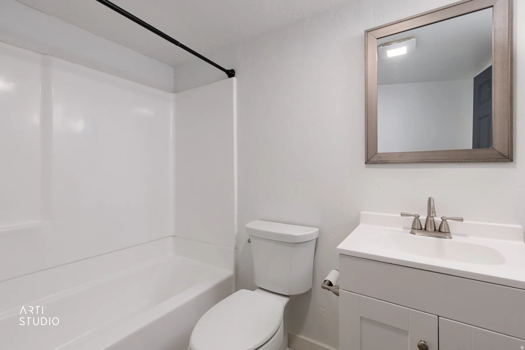 White bathtub with integrated shower, white vanity with integrated sink, brushed nickel faucet, framed wall mirror, and a white toilet