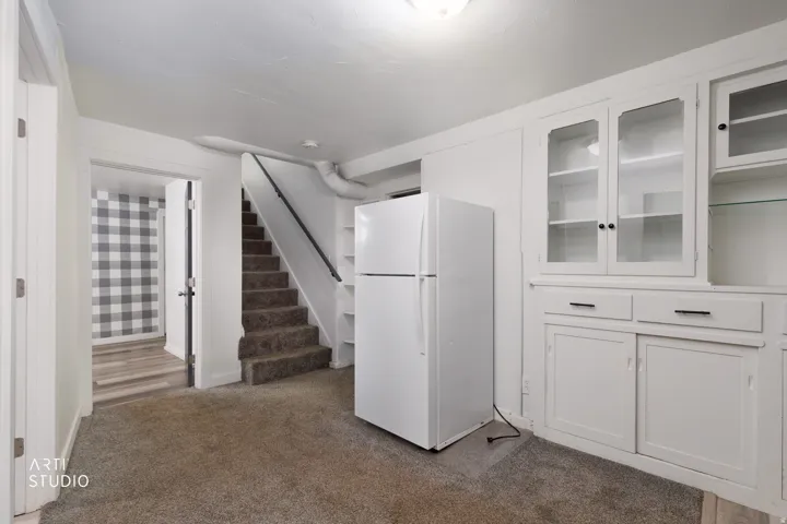 Built-in cabinetry with glass-front doors, neutral carpeting, and a stairway with a dark handrail