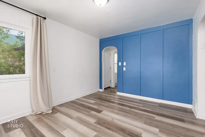 Wood-finish flooring, accent wall with paneling, white window trim, arched doorway, and overhead ceiling light fixture