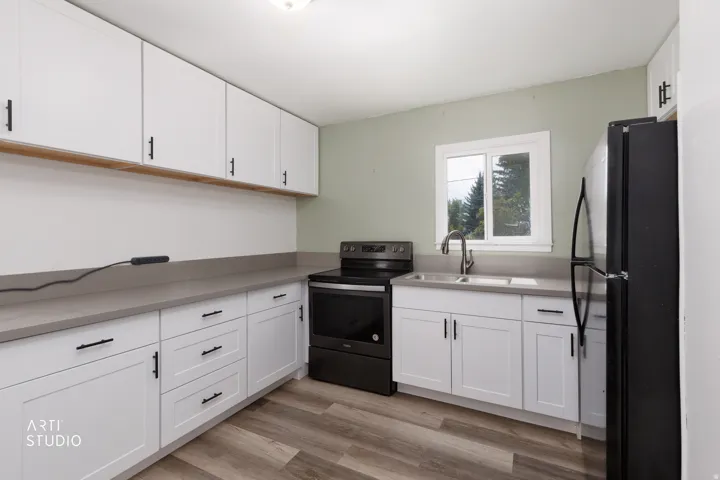 Kitchen featuring white shaker-style cabinetry, matte black hardware, integrated stainless steel sink, a full suite of black appliances, and wood-finish flooring