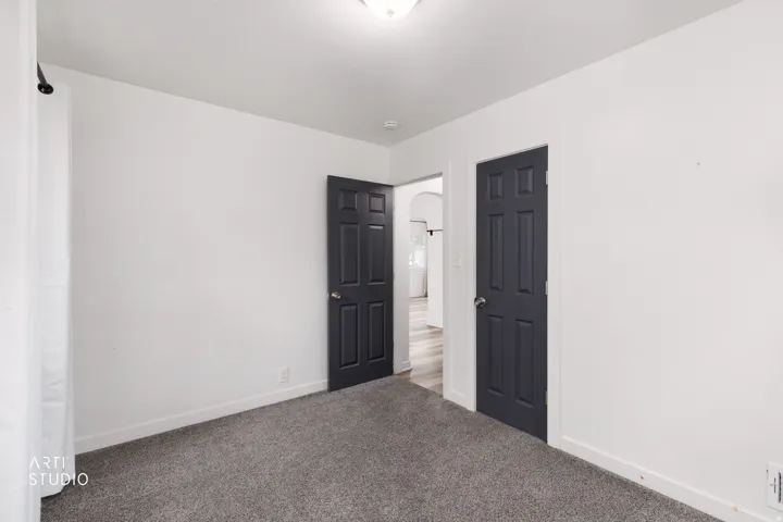 Interior room featuring light-toned walls, dark paneled doors, and grey carpeting