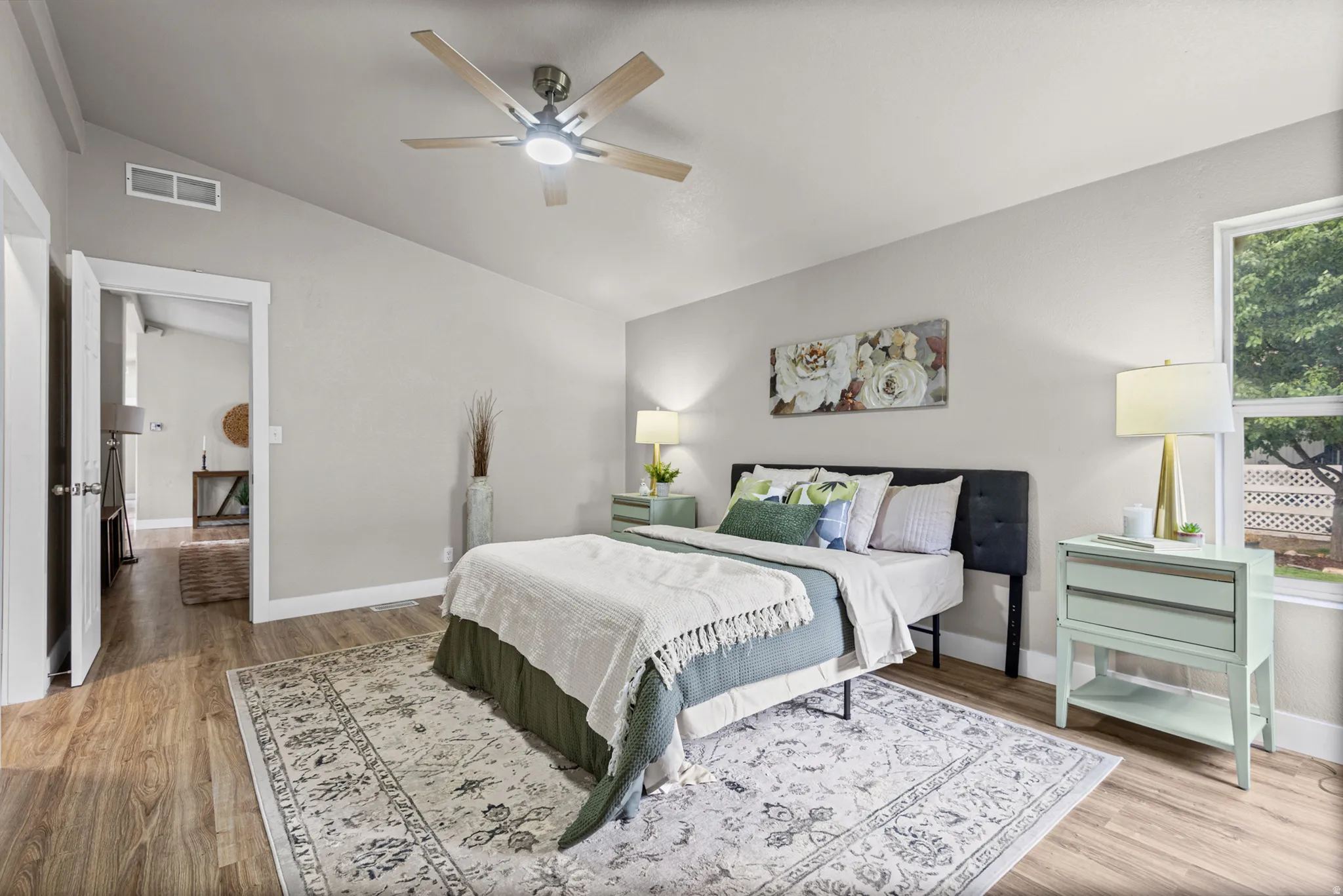 Wood-finish flooring, vaulted ceiling, ceiling fan with integrated lighting, window with exterior lattice, and neutral wall tones