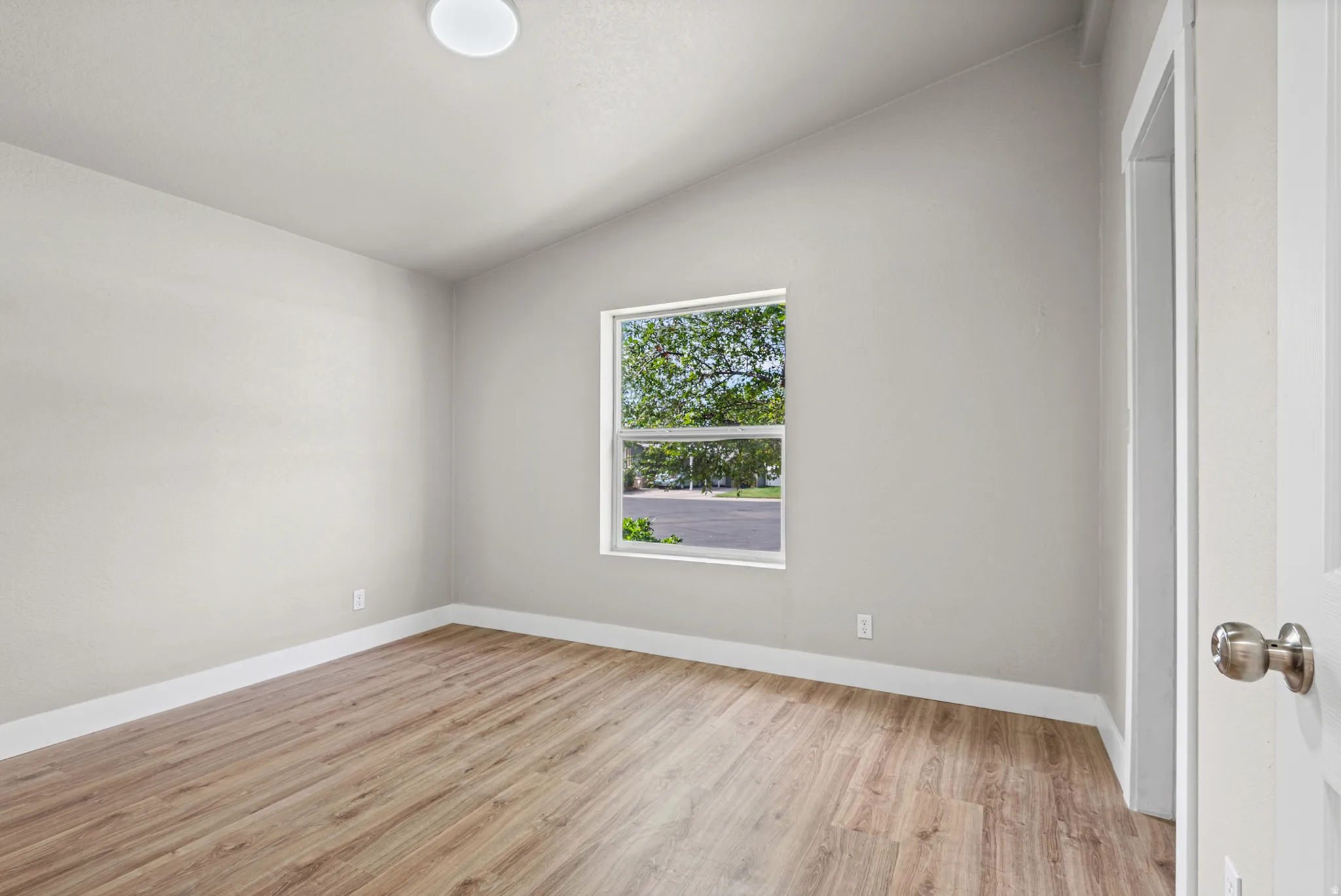 Vaulted ceiling, wood-finish flooring, white trim, recessed window, and flush mount lighting