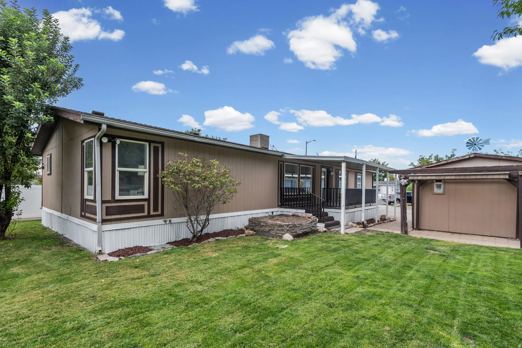 Expansive green lawn with mature trees, covered porch with railings, and a detached structure with a pitched roof