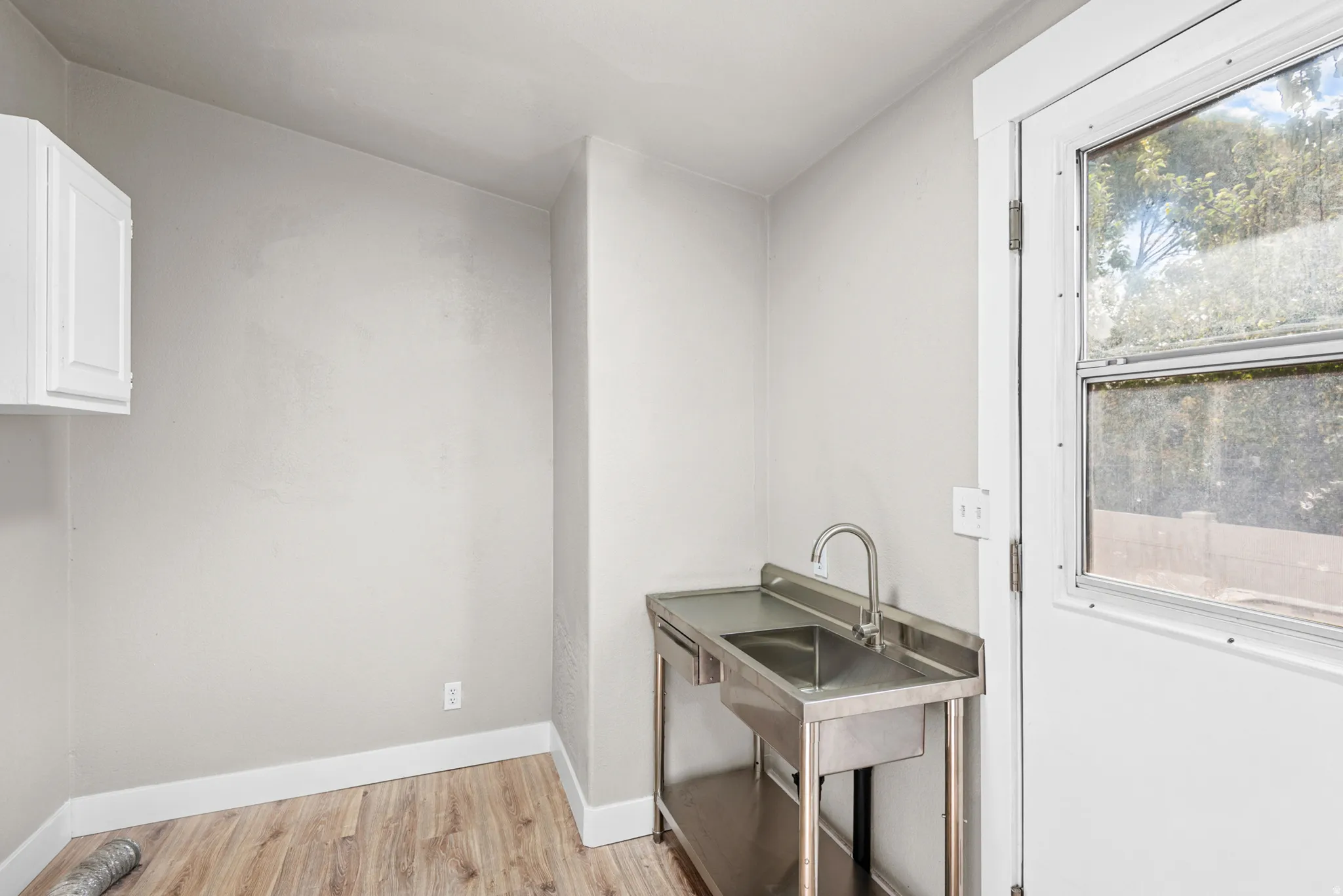 Stainless steel utility sink with a gooseneck faucet, white wall cabinetry, and wood-finish flooring