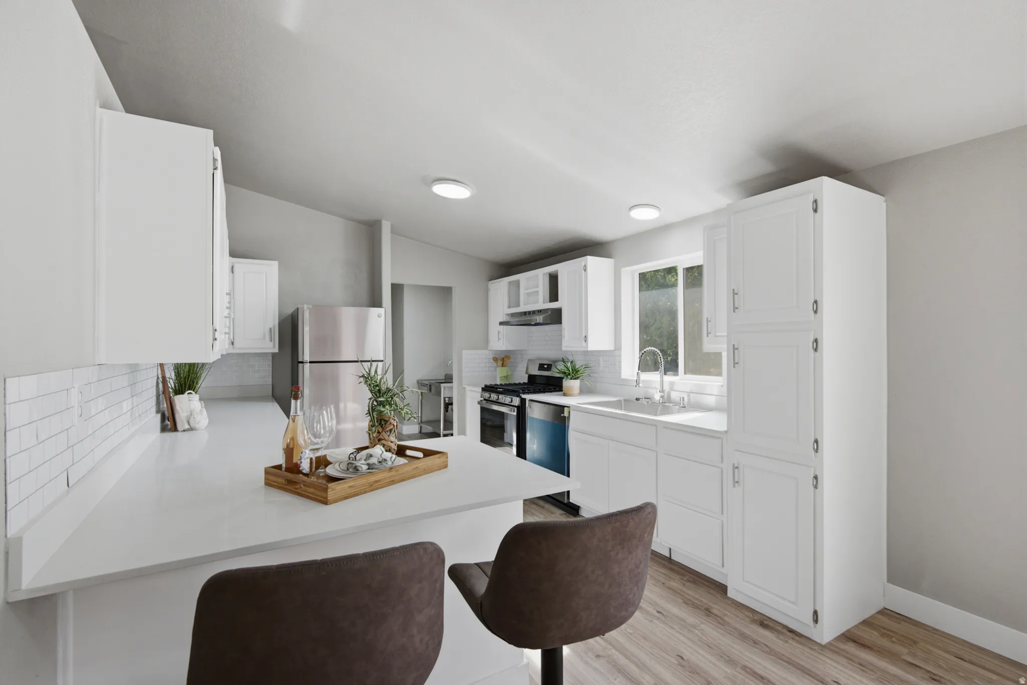 White shaker cabinetry, light-toned wood-finish flooring, white subway tile backsplash, stainless steel appliances, and recessed lighting